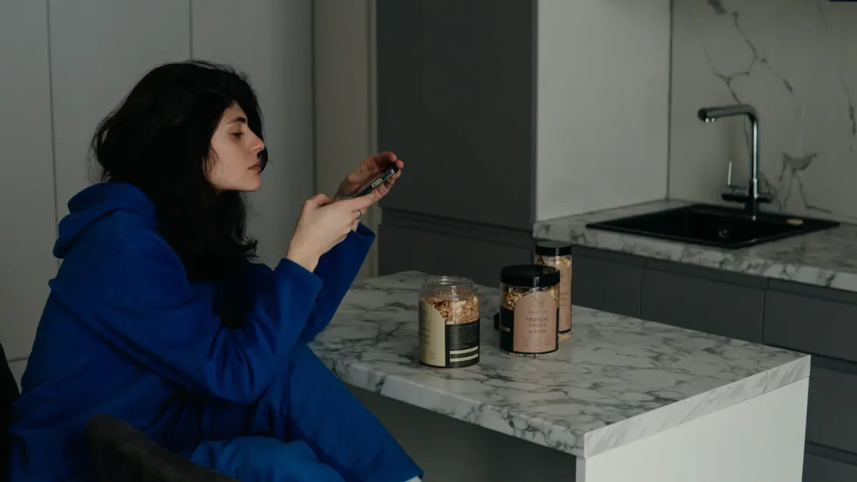 A dog owner reading the label on a supplement bottle at a kitchen counter, with a small terrier nearby